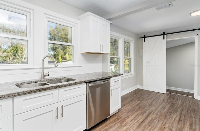 kitchen with sink, light stone counters, white cabinets, stainless steel dishwasher, and a barn door