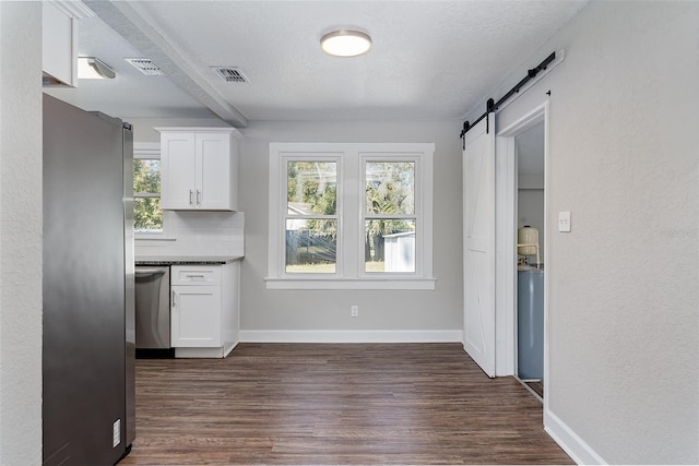 kitchen with backsplash, a barn door, white cabinets, and appliances with stainless steel finishes