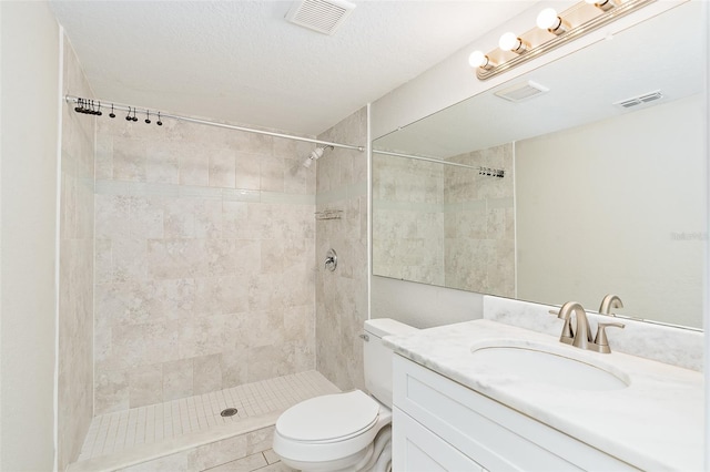 bathroom with vanity, a textured ceiling, toilet, and tiled shower