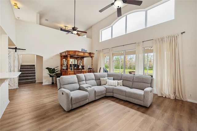 living room featuring light hardwood / wood-style floors, a barn door, ceiling fan, and a high ceiling