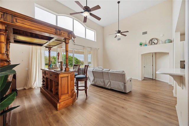 living room with a high ceiling, ceiling fan, and light wood-type flooring