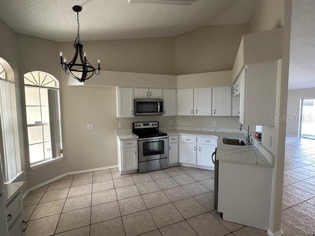 kitchen with hanging light fixtures, stainless steel appliances, white cabinets, light tile patterned flooring, and sink