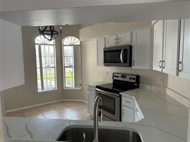 kitchen with decorative light fixtures, light stone counters, appliances with stainless steel finishes, white cabinets, and light tile patterned flooring