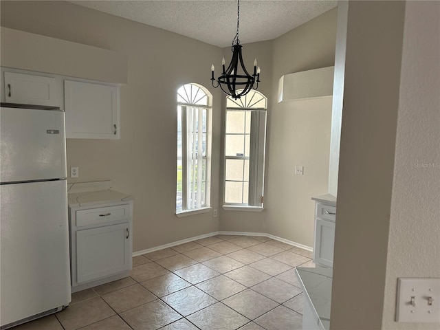 unfurnished dining area with a chandelier, light tile patterned flooring, a textured ceiling, decorative light fixtures, and white cabinets