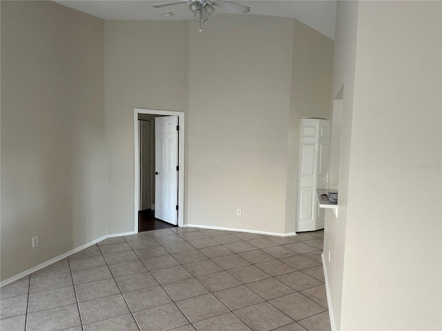 spare room featuring a towering ceiling, light tile patterned flooring, and ceiling fan