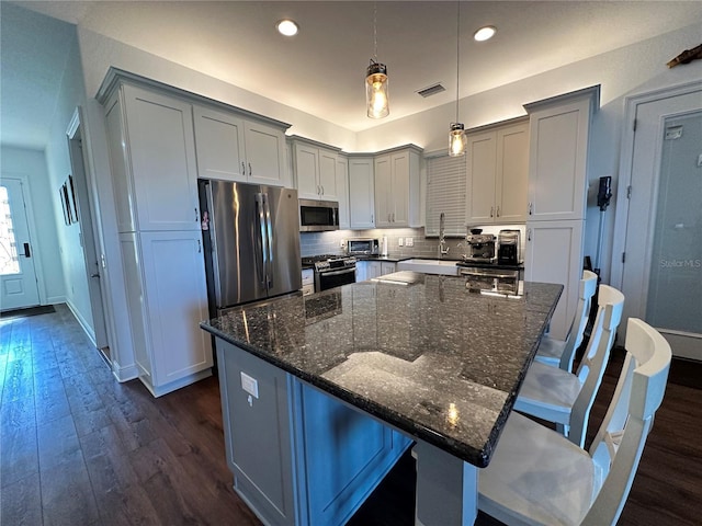 kitchen with dark stone countertops, a kitchen island, a breakfast bar, and appliances with stainless steel finishes