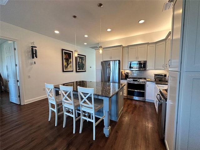 kitchen with a center island, hanging light fixtures, dark stone counters, a kitchen breakfast bar, and stainless steel appliances