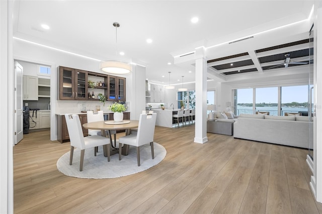 dining space with beamed ceiling, ornate columns, coffered ceiling, light wood-type flooring, and a water view