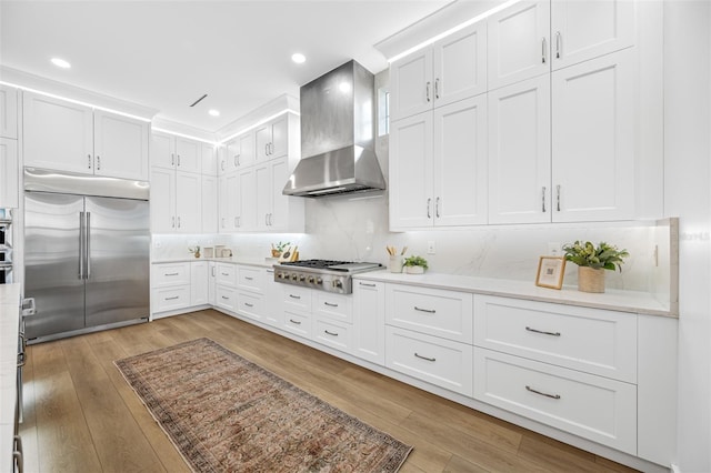 kitchen with light hardwood / wood-style floors, appliances with stainless steel finishes, tasteful backsplash, white cabinets, and wall chimney exhaust hood