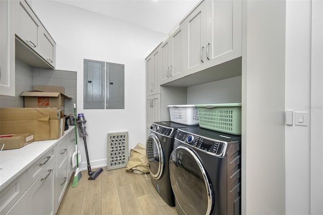 laundry area featuring electric panel, washer and clothes dryer, light hardwood / wood-style flooring, and cabinets