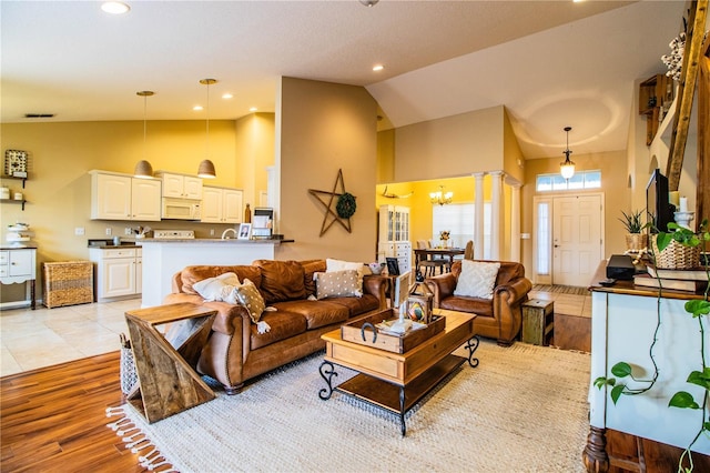 living room with decorative columns, high vaulted ceiling, an inviting chandelier, and light wood-type flooring