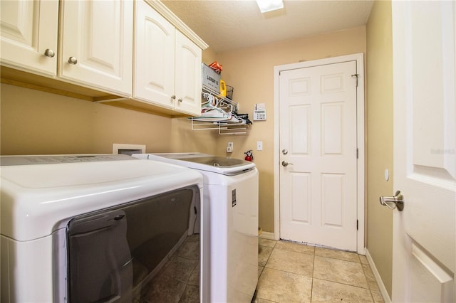 clothes washing area with cabinets, washer and dryer, a textured ceiling, and light tile patterned flooring