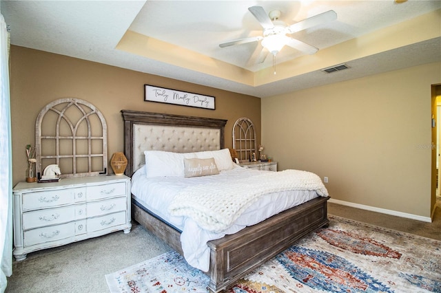 bedroom with ceiling fan, a tray ceiling, and light carpet