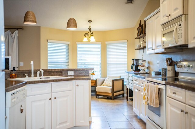 kitchen with light tile patterned floors, white cabinets, a sink, dark countertops, and white appliances