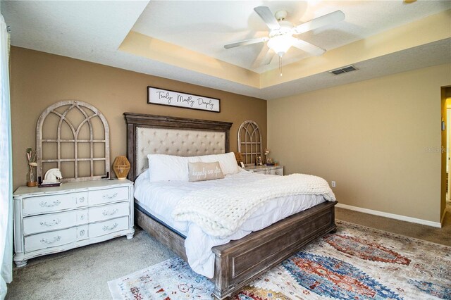 carpeted bedroom with ceiling fan, visible vents, baseboards, and a raised ceiling