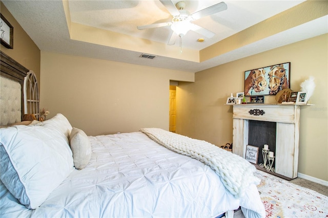 carpeted bedroom with baseboards, a fireplace, a ceiling fan, visible vents, and a raised ceiling