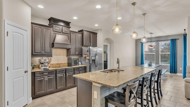 kitchen with stainless steel fridge, hanging light fixtures, sink, a kitchen bar, and a kitchen island with sink