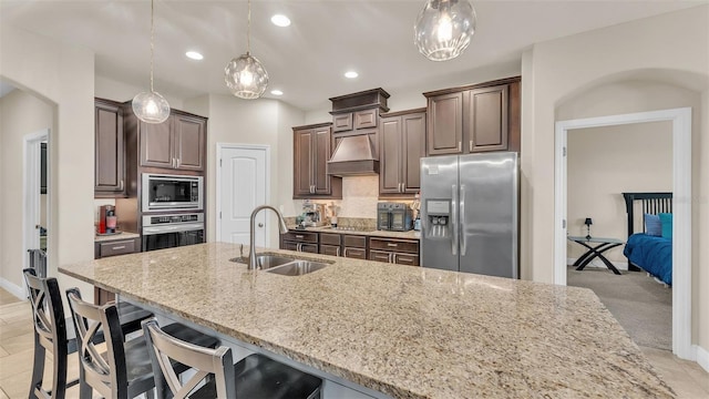 kitchen featuring appliances with stainless steel finishes, sink, decorative light fixtures, dark brown cabinets, and a center island with sink