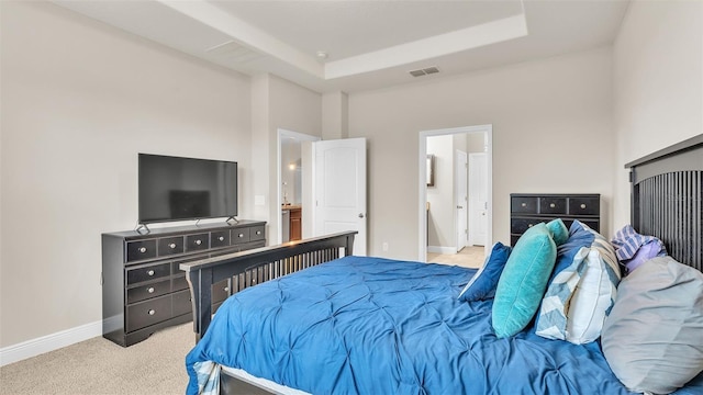 bedroom with connected bathroom, light carpet, and a tray ceiling