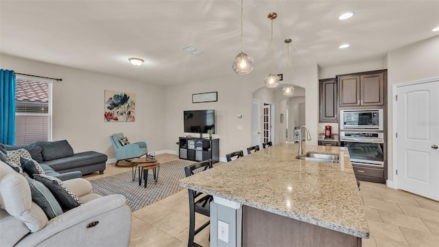 kitchen featuring dark brown cabinets, hanging light fixtures, sink, a breakfast bar, and stainless steel appliances