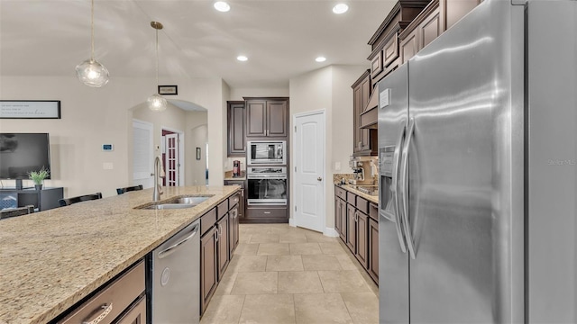 kitchen featuring light stone countertops, dark brown cabinetry, decorative light fixtures, stainless steel appliances, and sink