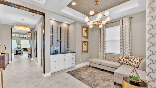 living room with ornamental molding, a raised ceiling, and ceiling fan with notable chandelier