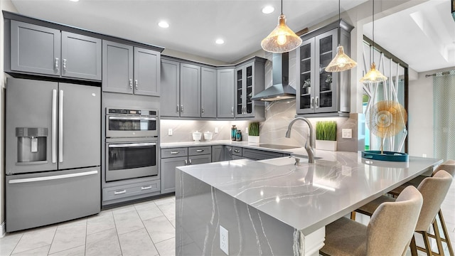 kitchen featuring stainless steel appliances, pendant lighting, gray cabinetry, and wall chimney range hood