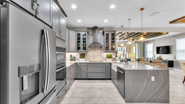 kitchen with wall chimney exhaust hood, sink, hanging light fixtures, stainless steel appliances, and backsplash