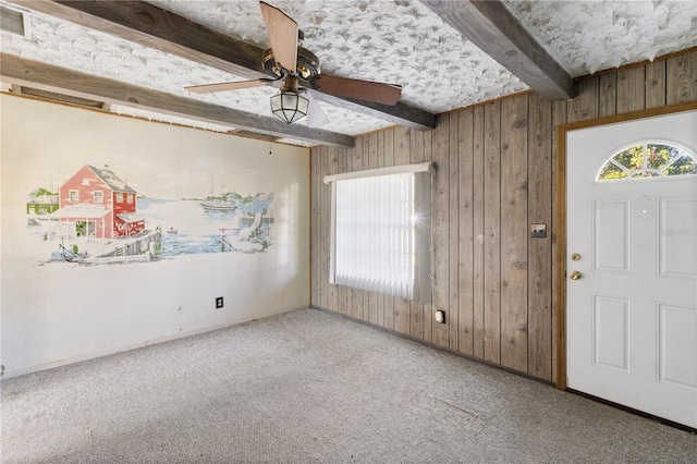 foyer with ceiling fan, wooden walls, beam ceiling, and carpet floors