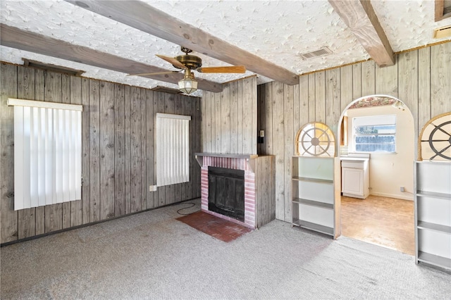 unfurnished living room with a brick fireplace, beam ceiling, carpet floors, and ceiling fan