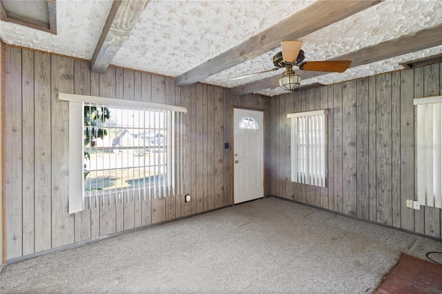 interior space with beam ceiling, ceiling fan, and wood walls