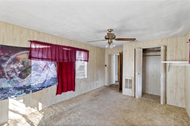 unfurnished bedroom featuring a closet, wood walls, ceiling fan, and carpet