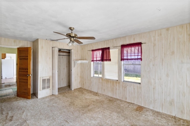 unfurnished bedroom featuring white refrigerator, carpet flooring, ceiling fan, and wood walls