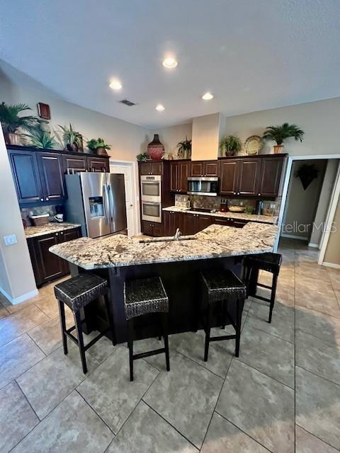 kitchen featuring a spacious island, light stone countertops, stainless steel appliances, and a breakfast bar