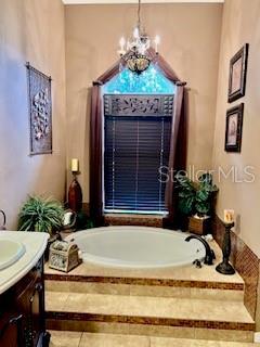 bathroom with tiled bath, vanity, and an inviting chandelier