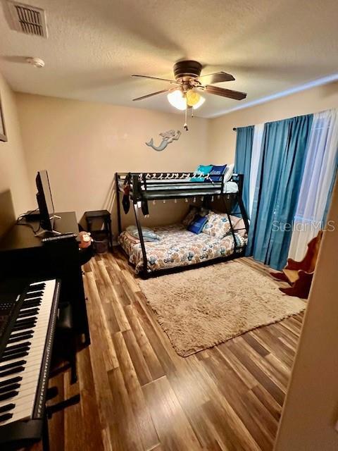 bedroom with ceiling fan, wood-type flooring, and a textured ceiling