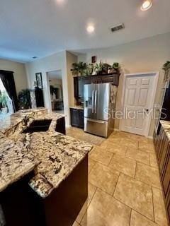 kitchen with sink, light stone countertops, stainless steel fridge with ice dispenser, and dark brown cabinetry