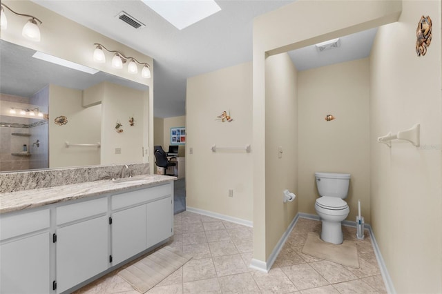 bathroom with a skylight, tiled shower, vanity, tile patterned floors, and toilet