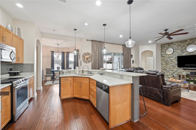 kitchen featuring appliances with stainless steel finishes, sink, hanging light fixtures, light stone counters, and a breakfast bar