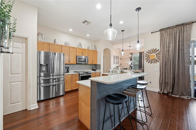 kitchen featuring light stone countertops, decorative light fixtures, stainless steel appliances, a center island with sink, and a breakfast bar area