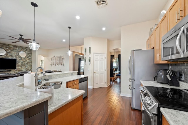 kitchen with hanging light fixtures, sink, dark wood-type flooring, stainless steel appliances, and light stone counters