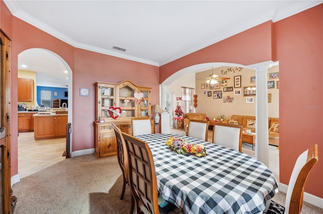 dining space with crown molding, light carpet, ceiling fan, and decorative columns