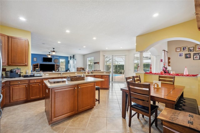 kitchen featuring kitchen peninsula, ceiling fan, light tile patterned flooring, a center island, and decorative columns