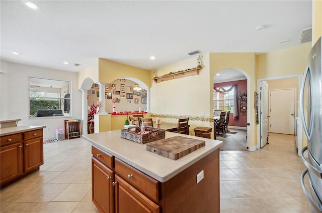 kitchen with stainless steel refrigerator, light tile patterned floors, ornate columns, and a kitchen island