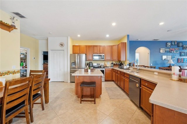 kitchen featuring a kitchen breakfast bar, sink, light tile patterned floors, a kitchen island, and stainless steel appliances