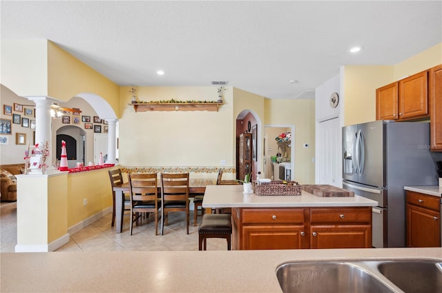 kitchen featuring a center island, decorative columns, light tile patterned floors, a breakfast bar, and stainless steel fridge