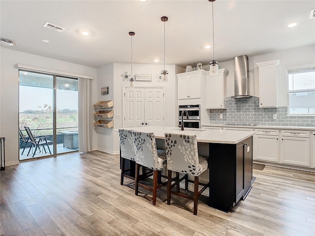 kitchen with wall chimney exhaust hood, pendant lighting, and an island with sink