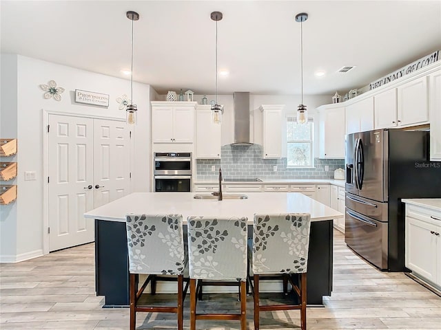 kitchen featuring hanging light fixtures, a kitchen island with sink, wall chimney range hood, sink, and stainless steel appliances