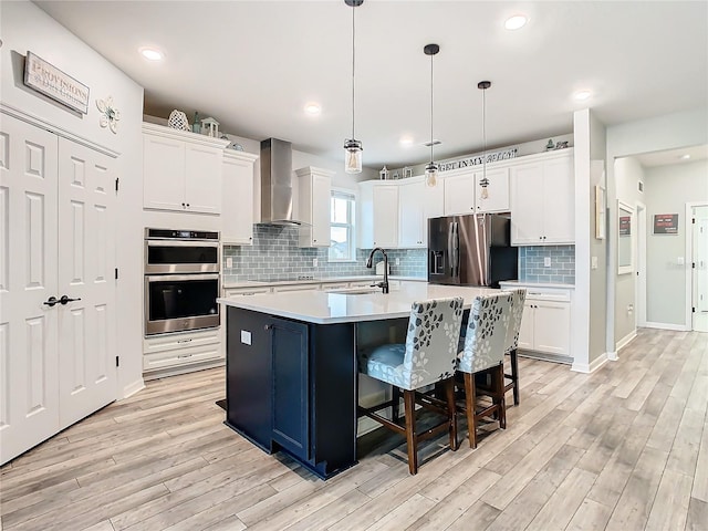 kitchen featuring wall chimney exhaust hood, a kitchen island with sink, white cabinetry, and appliances with stainless steel finishes