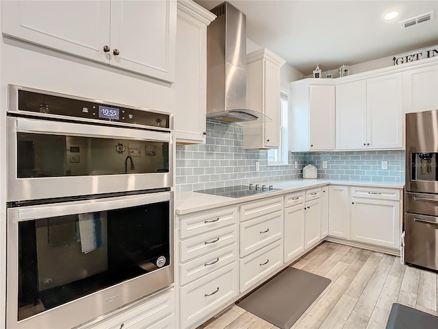 kitchen with wall chimney range hood, white cabinets, appliances with stainless steel finishes, and tasteful backsplash